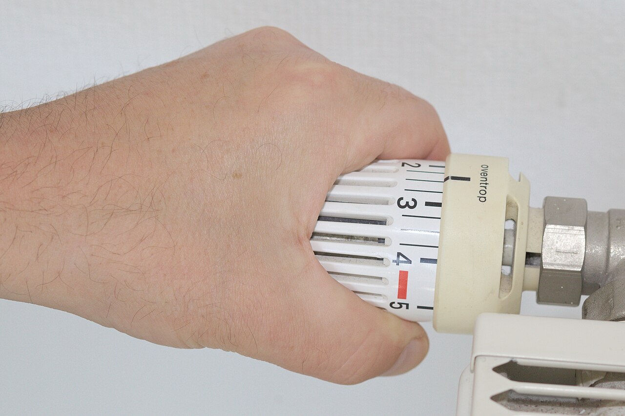 A hand turning the thermostatic valve on a home radiator