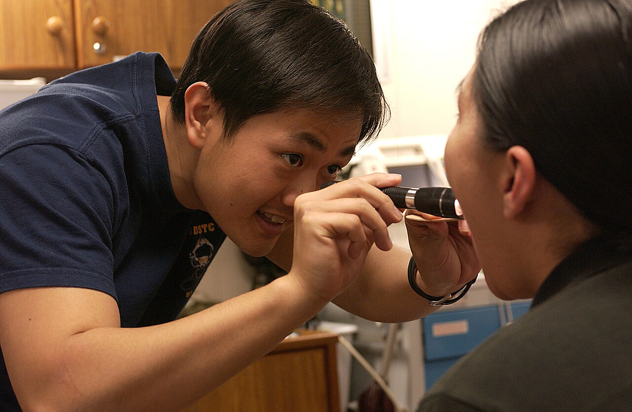 A doctor shines a small torch into a patient’s open mouth to examine the throat