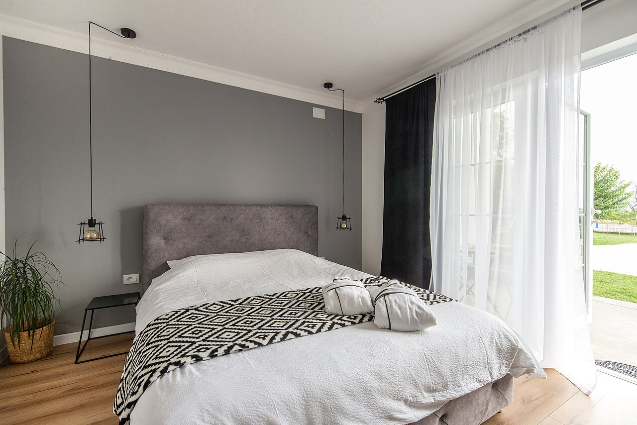 A made bed in a bedroom, with daylight coming through an open patio door