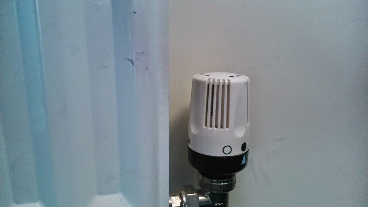 A white thermostatic valve fitted to a radiator beside a wall