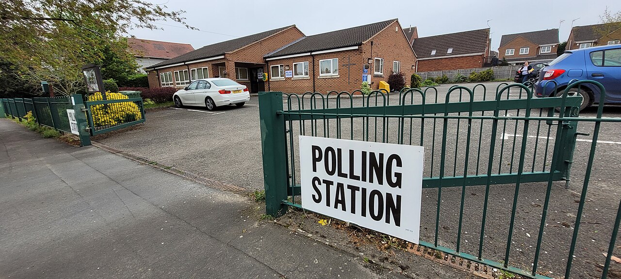 A polling station sign on green railings outside a community building during the 2024 local elections