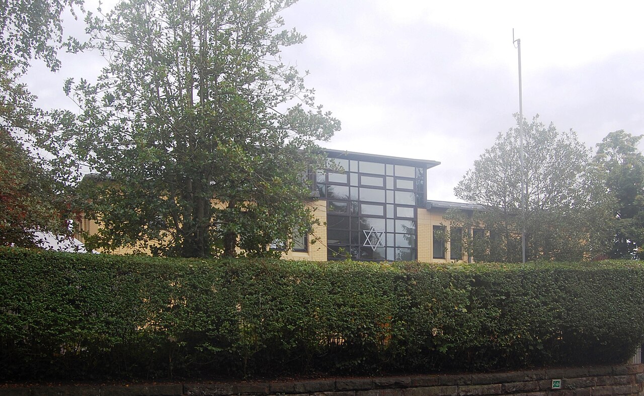 A synagogue in Greater Manchester with a Star of David on its glass frontage, seen over a hedge
