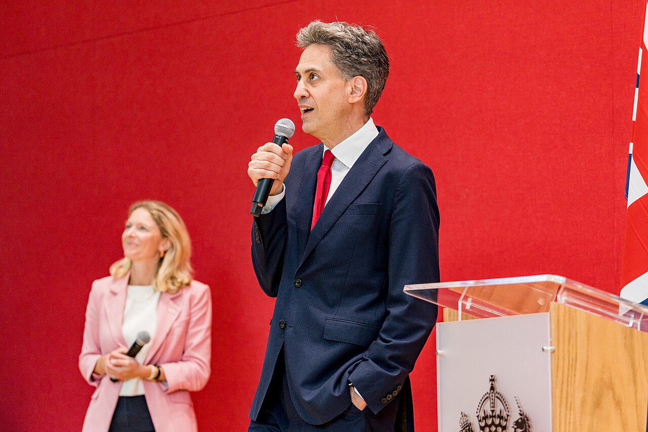 Foreign Secretary Ed Miliband speaking into a microphone beside a lectern and a Union flag