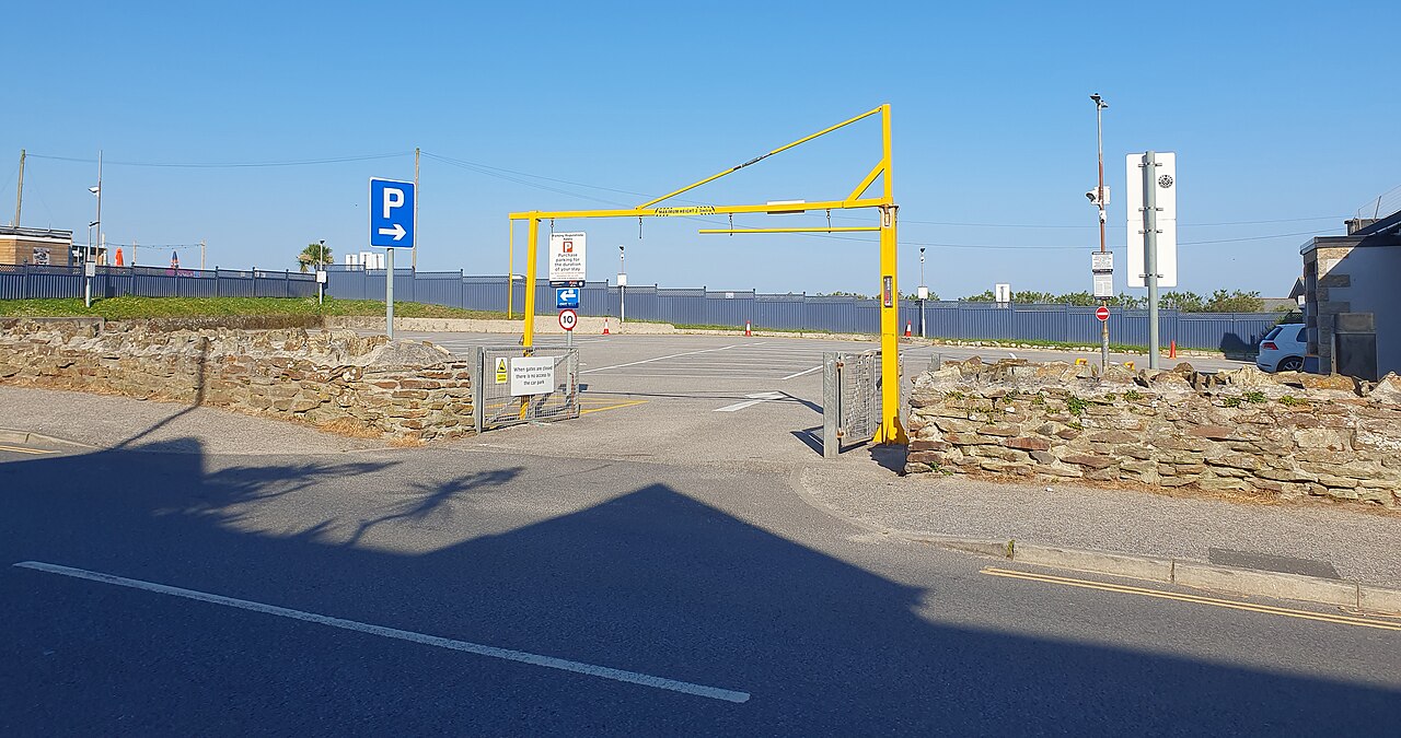 The entrance to a car park in Newquay, Cornwall, with a yellow height barrier and a blue parking sign