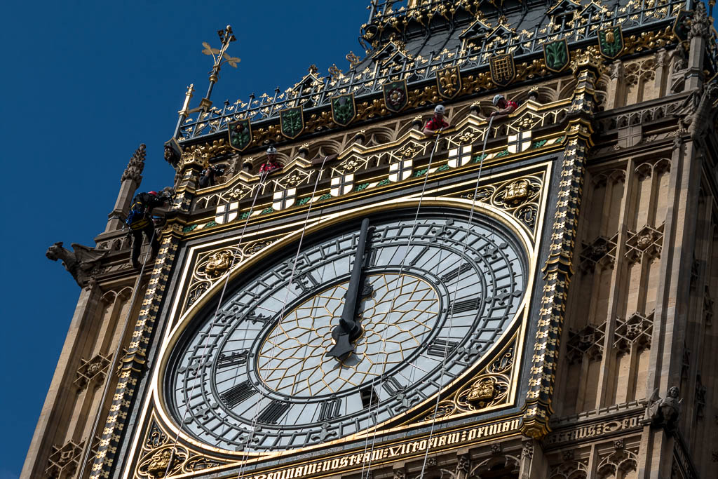 Abseiling cleaners on ropes beside the clock face of Elizabeth Tower, home of Big Ben, with the hands pointing to just after twelve