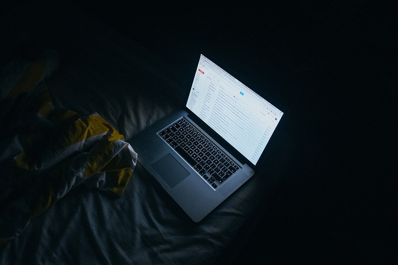 A laptop screen glowing in a dark bedroom, the only light in the room