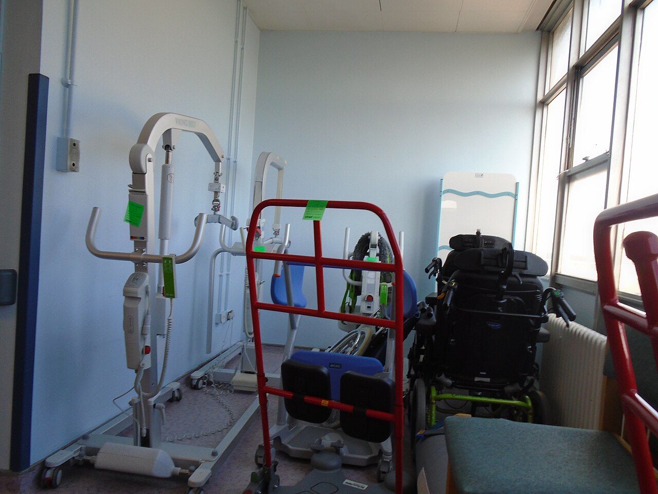 A mobile patient hoist and wheelchair stored in a hospital corridor