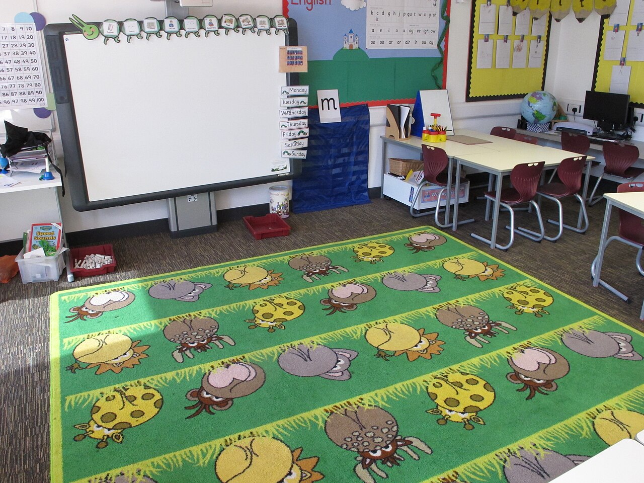 An empty primary school classroom with a colourful floor rug and an interactive whiteboard