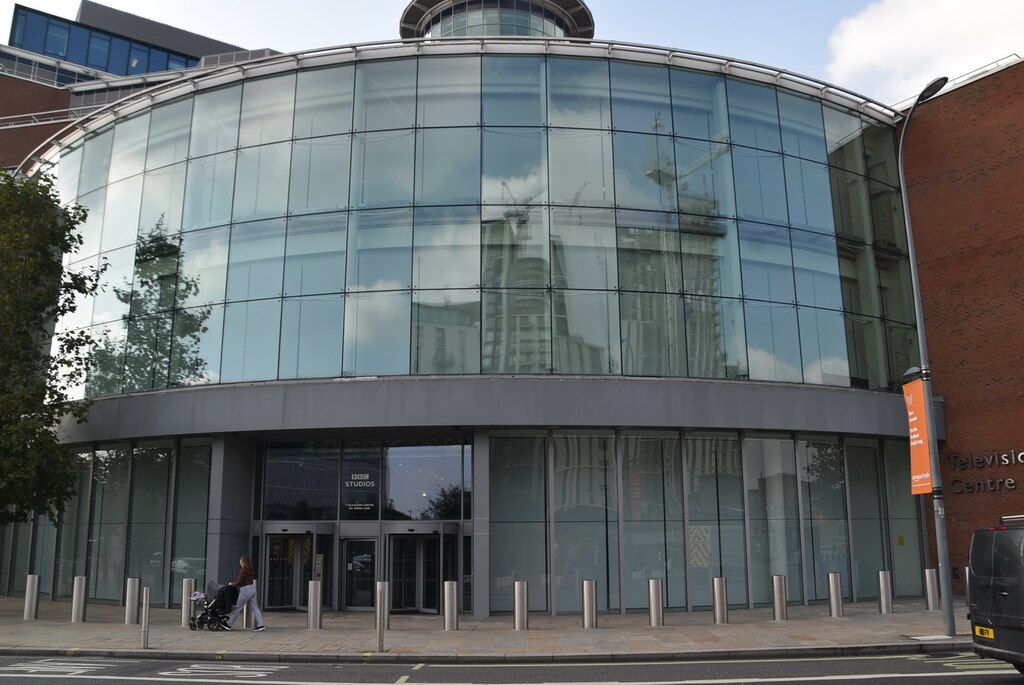 The curved glass front of BBC Television Centre in west London, with a pedestrian pushing a pushchair past the entrance