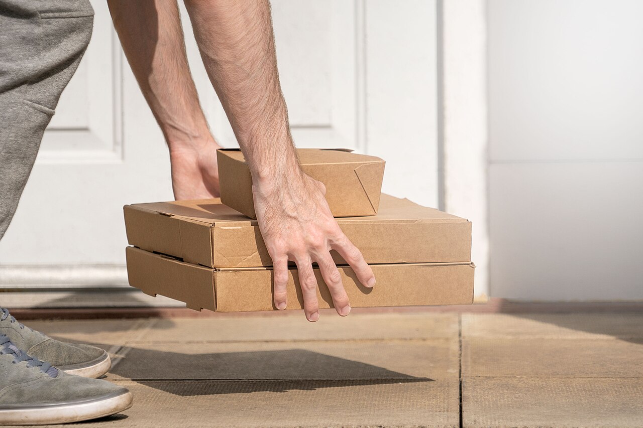 A person placing three cardboard takeaway boxes on a doorstep in front of a white door