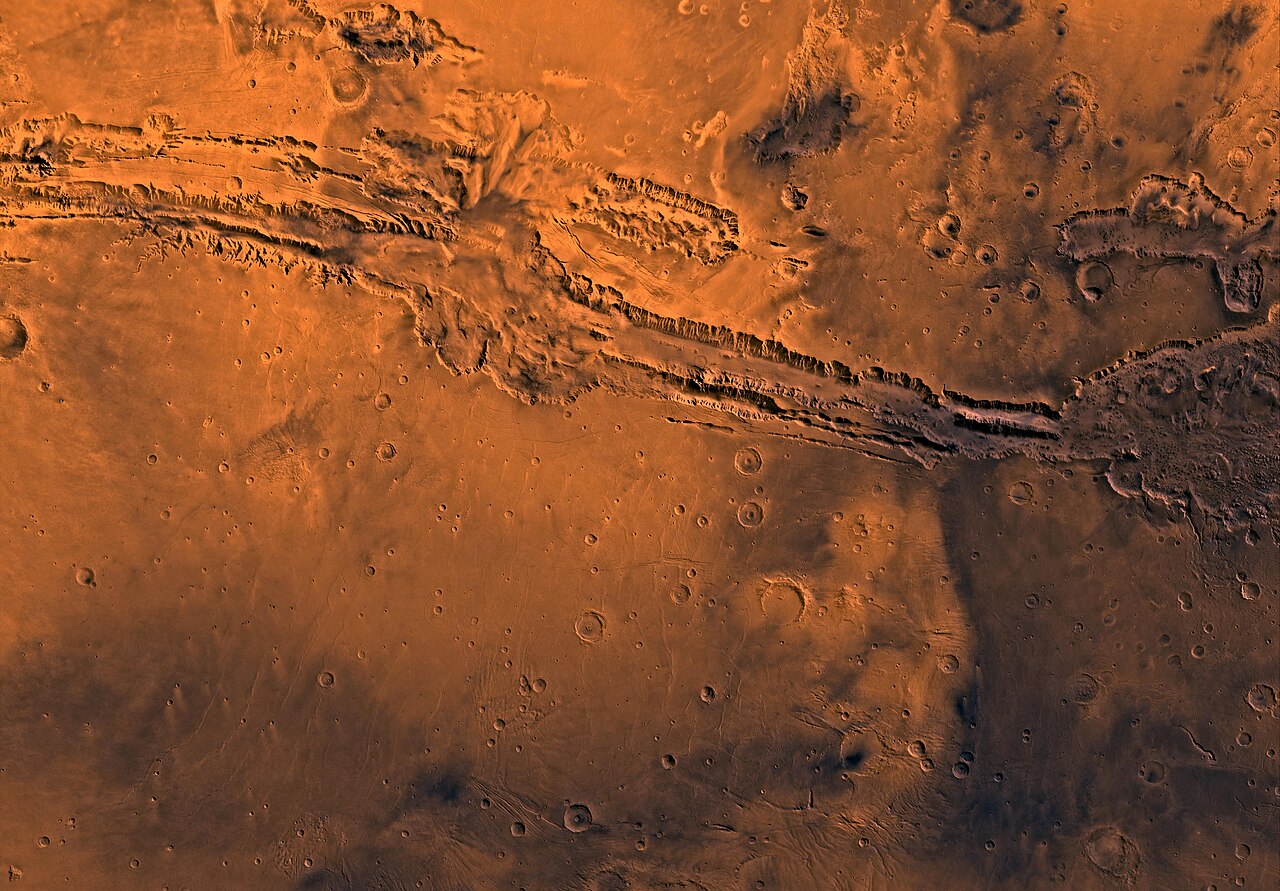 Orbiter mosaic of the Valles Marineris canyon system running across the orange Martian surface, with craters on either side.