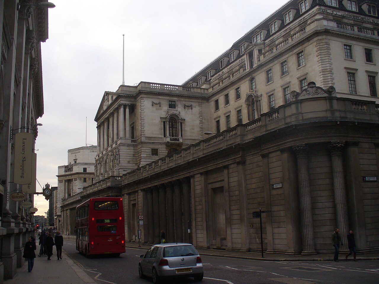 The Bank of England building on Threadneedle Street in the City of London, with a red double-decker bus and a car in the road.