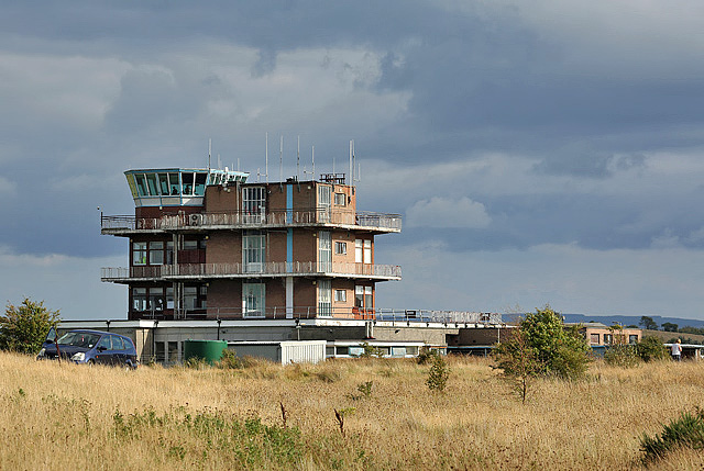 The air traffic control tower at Glasgow Prestwick Airport in Scotland, seen across open grassland under a cloudy sky.