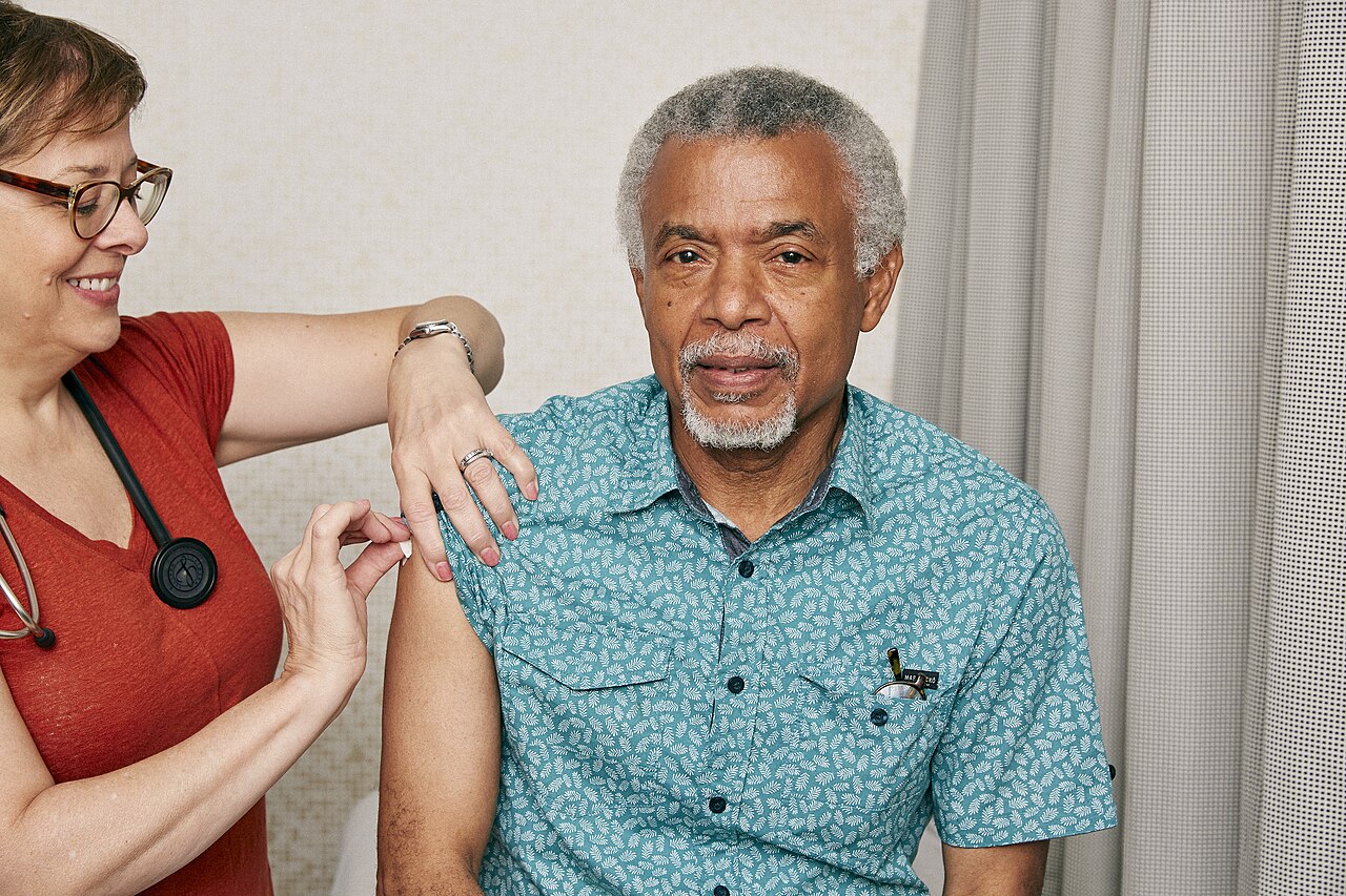 An older man has his upper arm cleaned before an injection