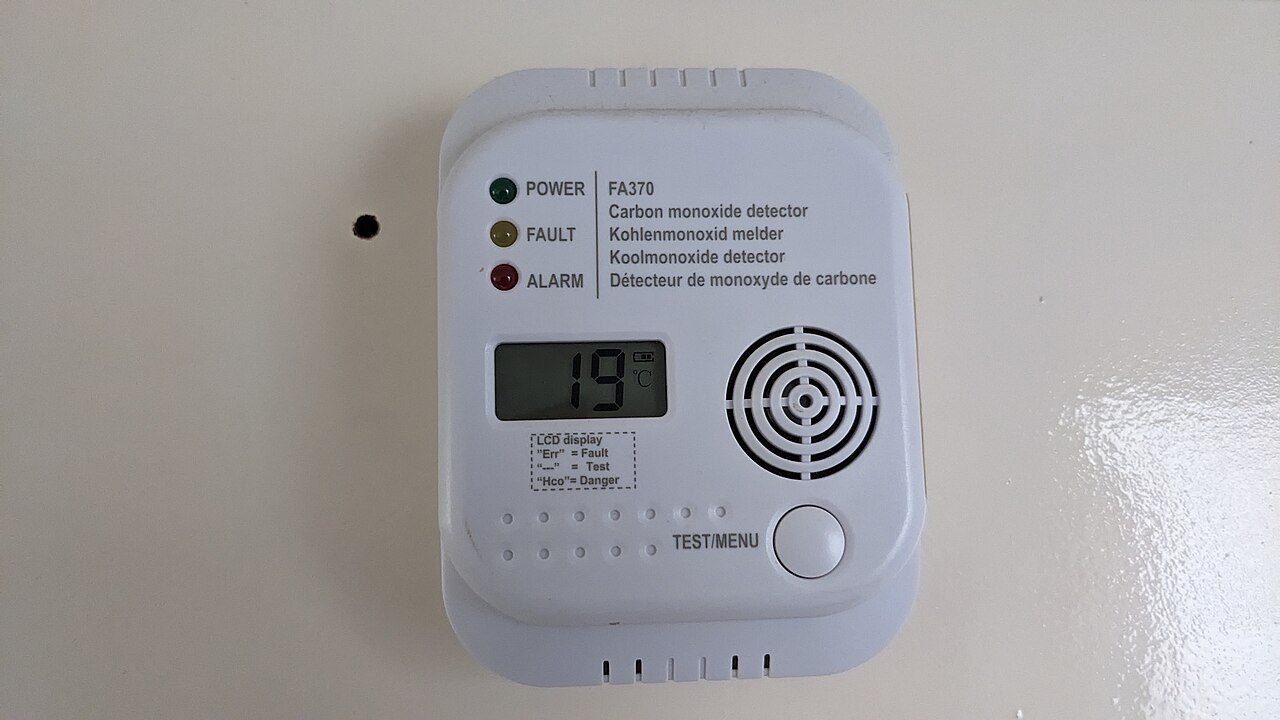 A white wall-mounted carbon monoxide detector with a small display, three indicator lights and a test button