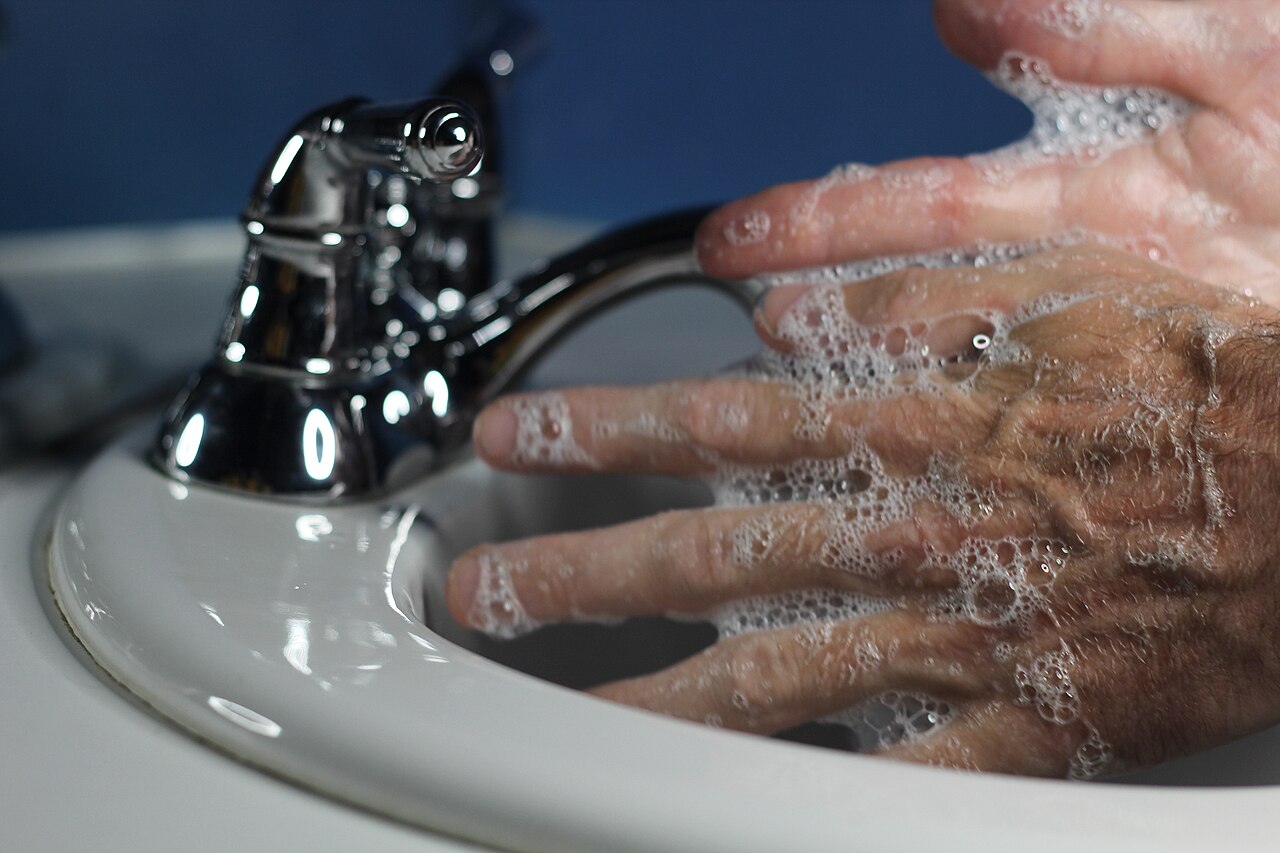 A man’s soapy hands in a white sink beside a chrome tap