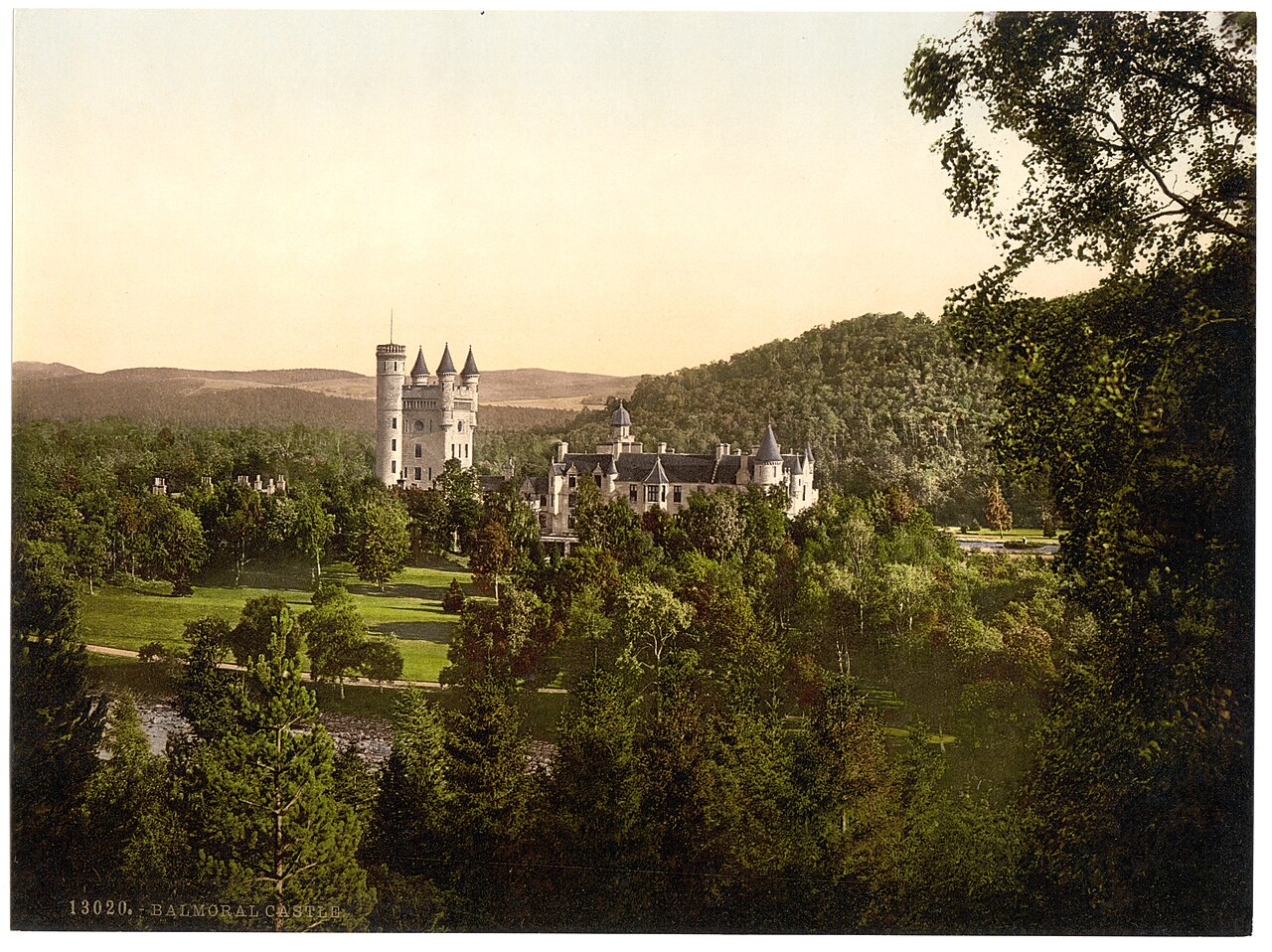 Balmoral Castle in Aberdeenshire seen across trees and parkland, in a colour photograph from the 1890s labelled Balmoral Castle