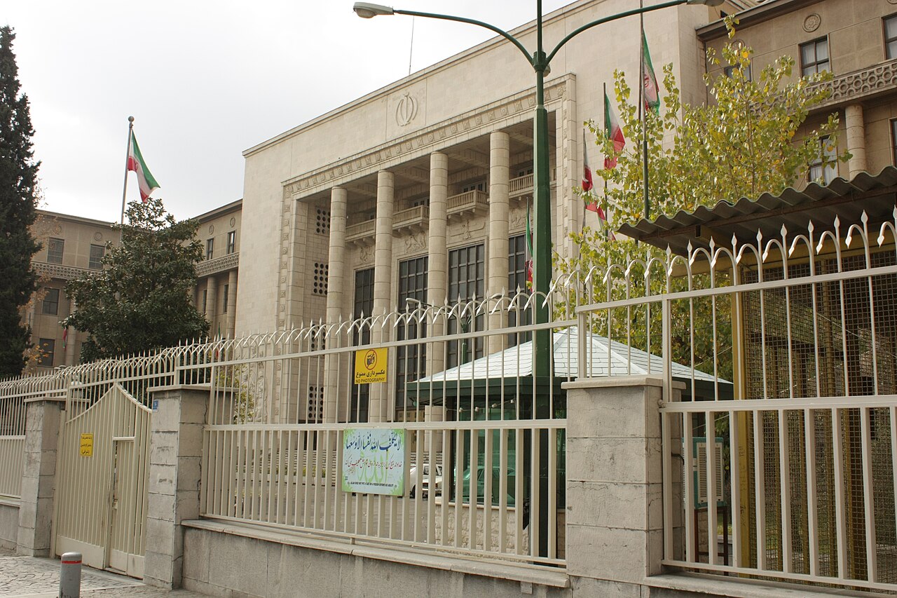 The Tehran Courthouse, a columned stone building behind a fence with Iranian flags and a yellow ‘No photography’ sign. The case in this story was heard in Mashhad.