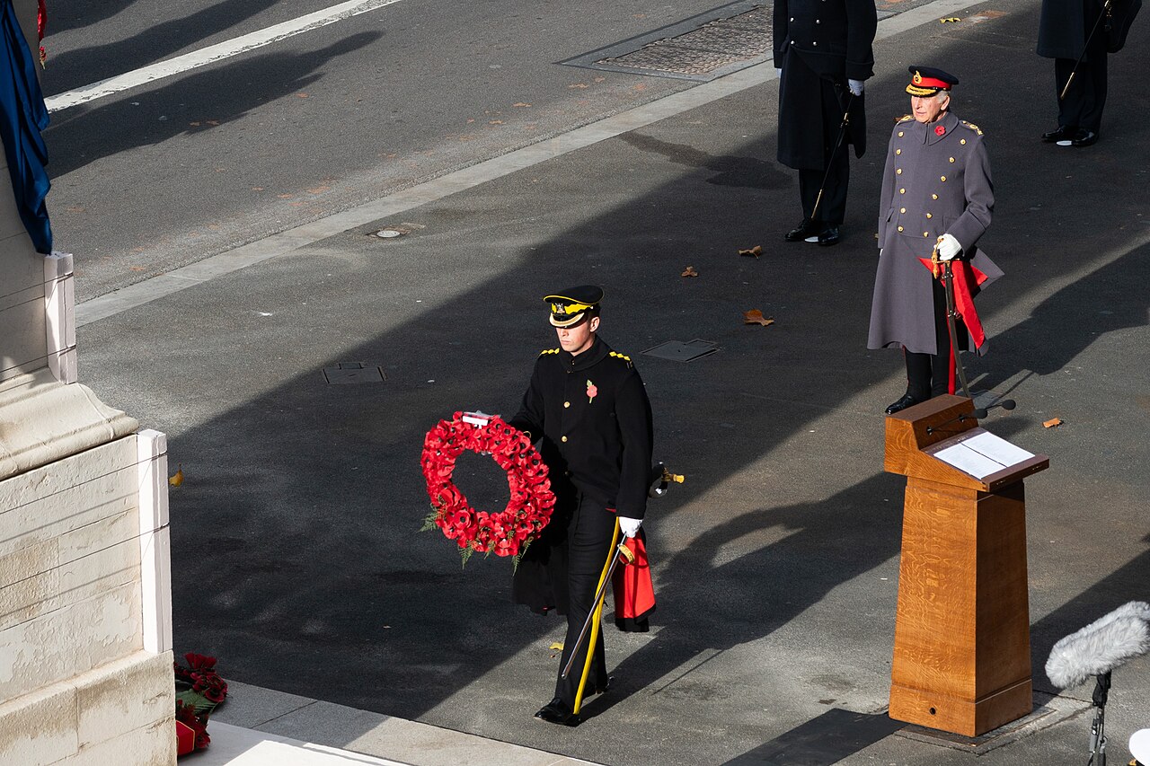 A uniformed officer carries a red poppy wreath beside the Cenotaph in Whitehall during the 2025 Remembrance Sunday service