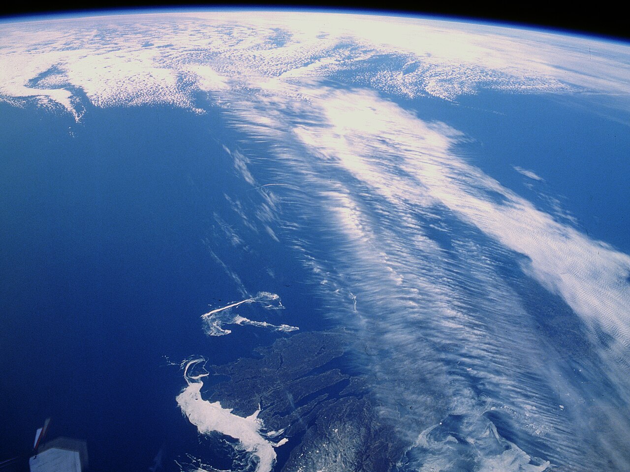 A photograph taken from orbit shows long streaks of high cloud sweeping across the sea and coast of eastern Canada beneath the curve of the Earth, a view of the jet stream