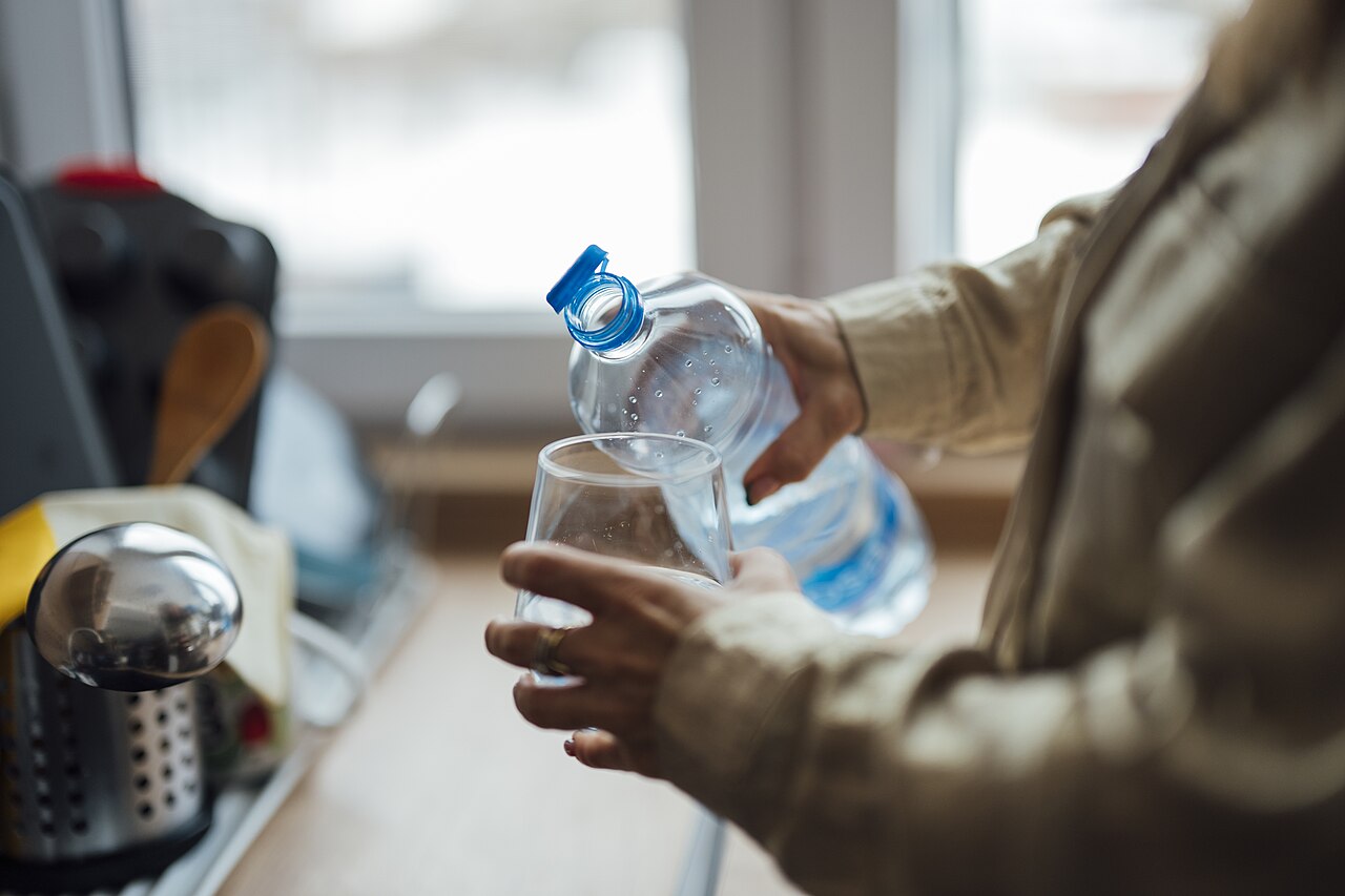 A person pours water from a bottle into a glass in a kitchen