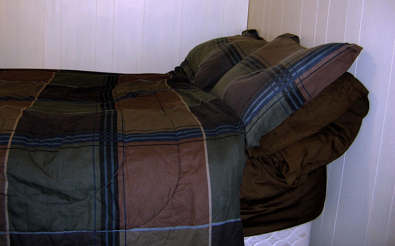 A bed with plaid bedding and stacked pillows against a white wall