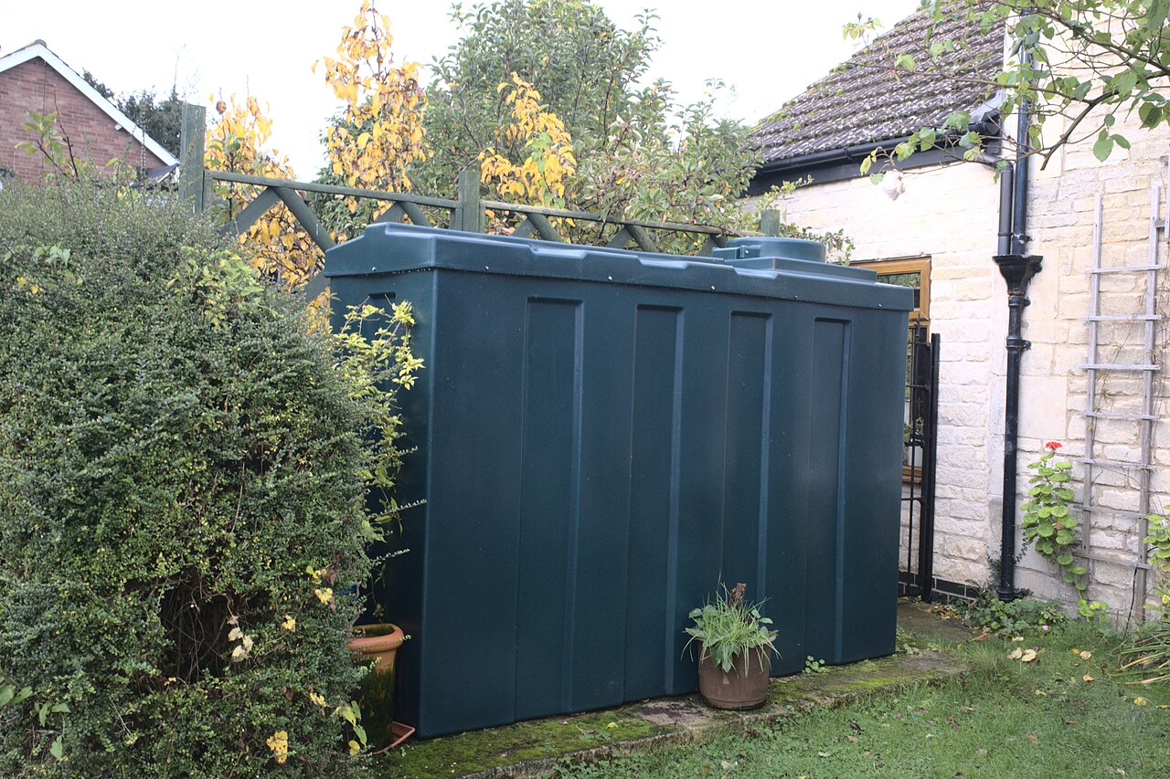 A dark green plastic oil tank beside the wall of a house in a garden