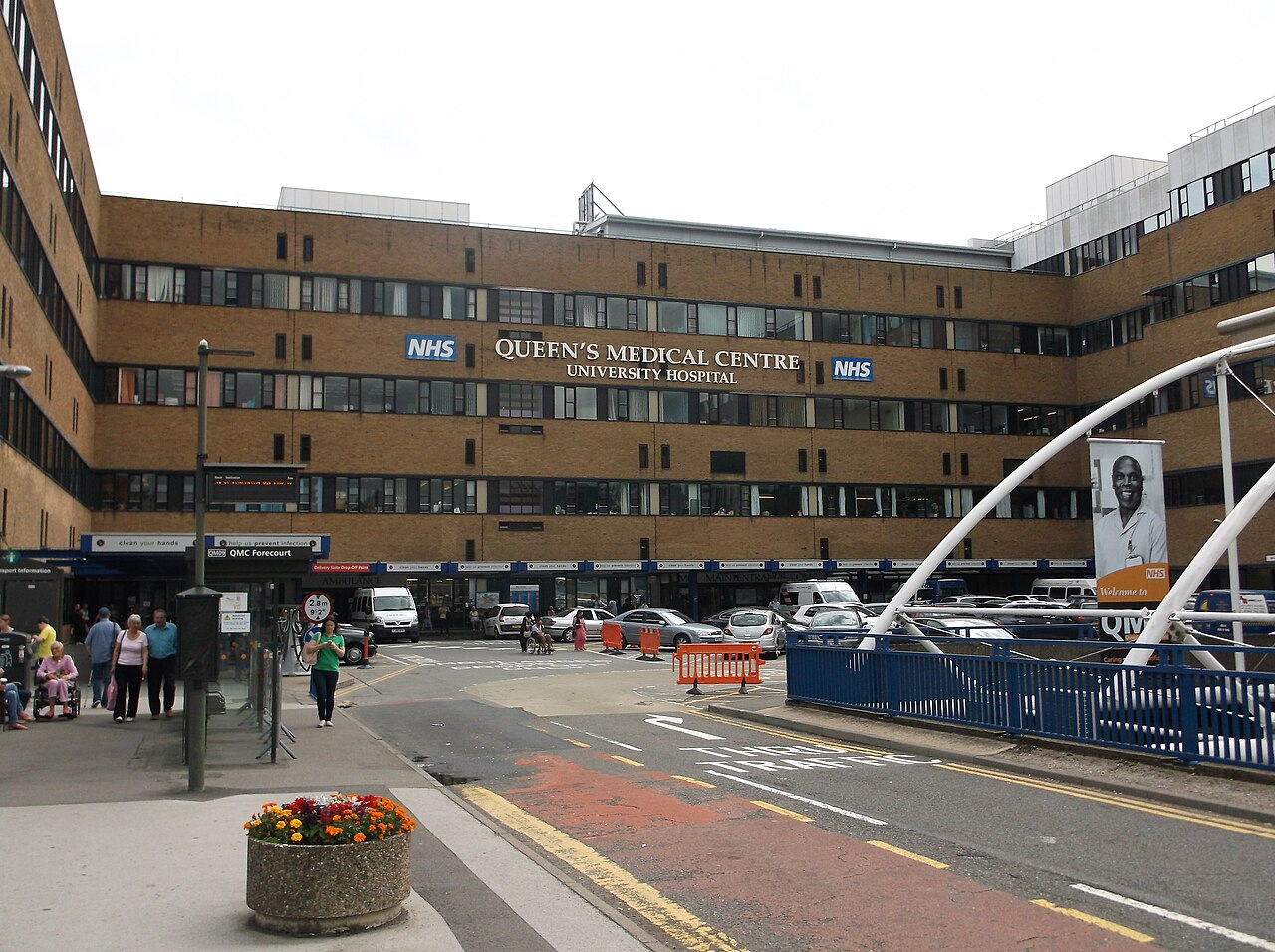 The front of Queen's Medical Centre University Hospital in Nottingham, with NHS logos on the brick wall and a few people on the pavement