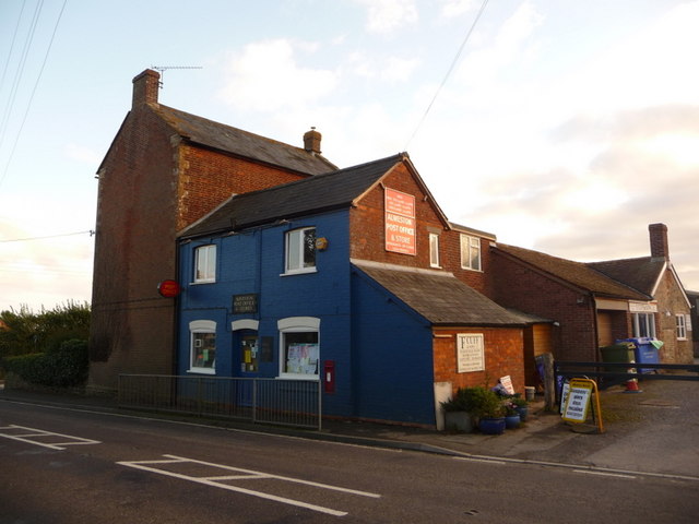 A village post office and shop in a blue-painted building on an English roadside, with a red post box by the door.