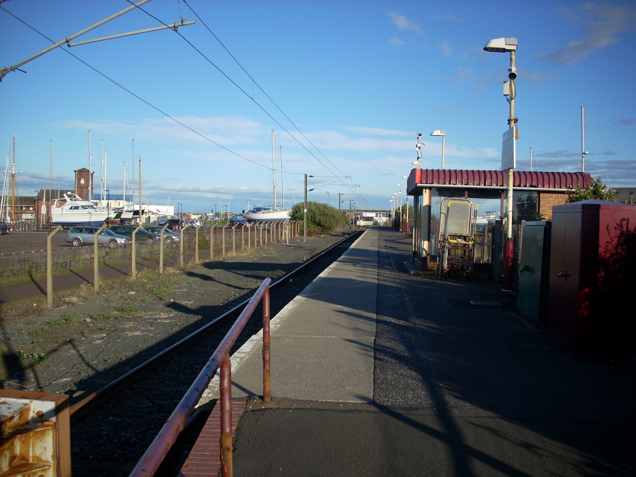 Platform and track at Ardrossan Harbour railway station in North Ayrshire, Scotland, with moored boats beyond the fence