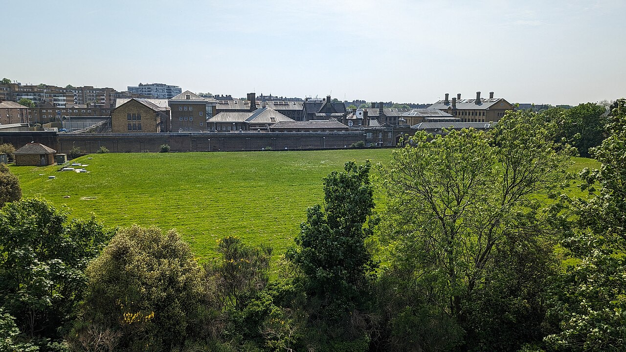 Brick buildings and perimeter wall of HMP Brixton in south London, seen across a grass field from the nearby Brixton Windmill