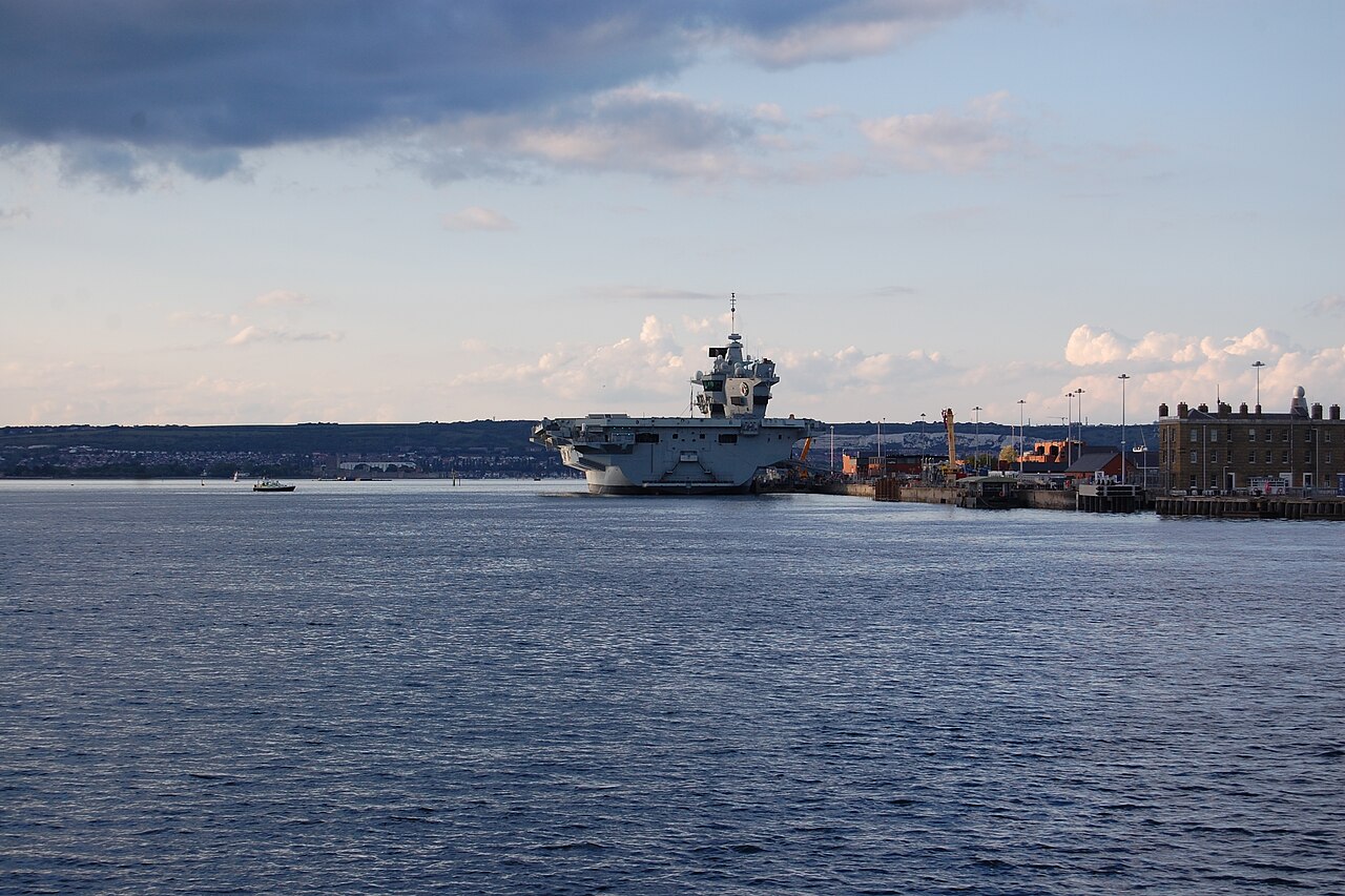 The aircraft carrier HMS Queen Elizabeth moored at Portsmouth Harbour in England under a partly cloudy sky