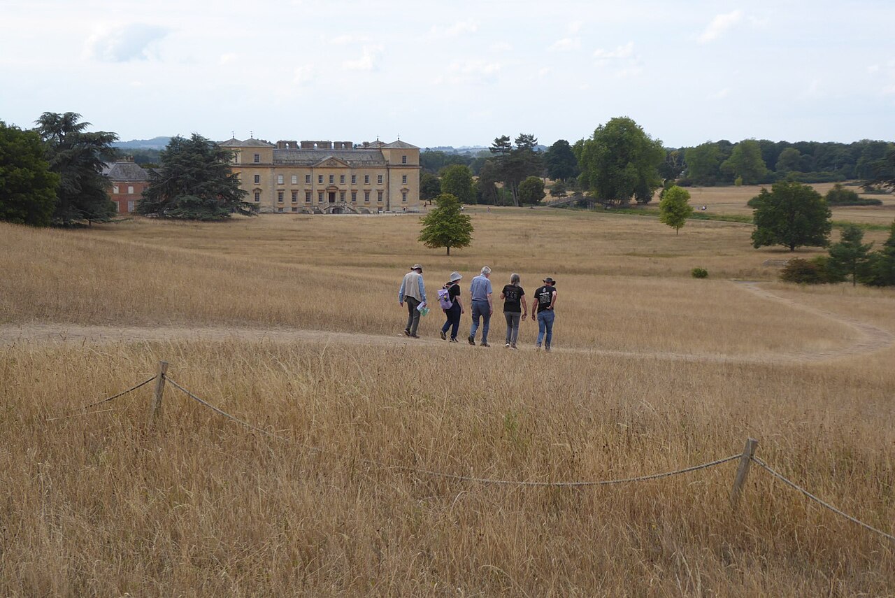 Five people walking along a path across open parkland, with a country house in the distance
