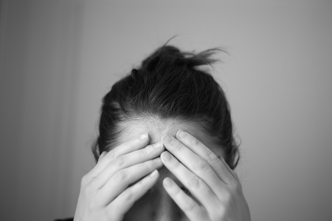 A person with their hands pressed to their forehead, head bowed, in a black-and-white photograph
