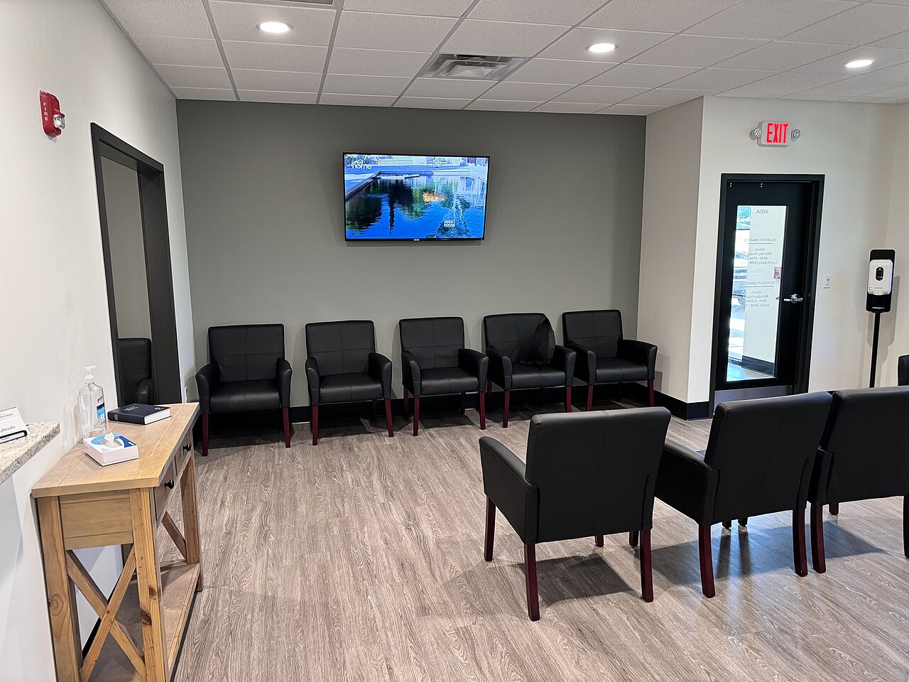 Rows of dark armchairs in an empty clinic waiting room with a wall-mounted television