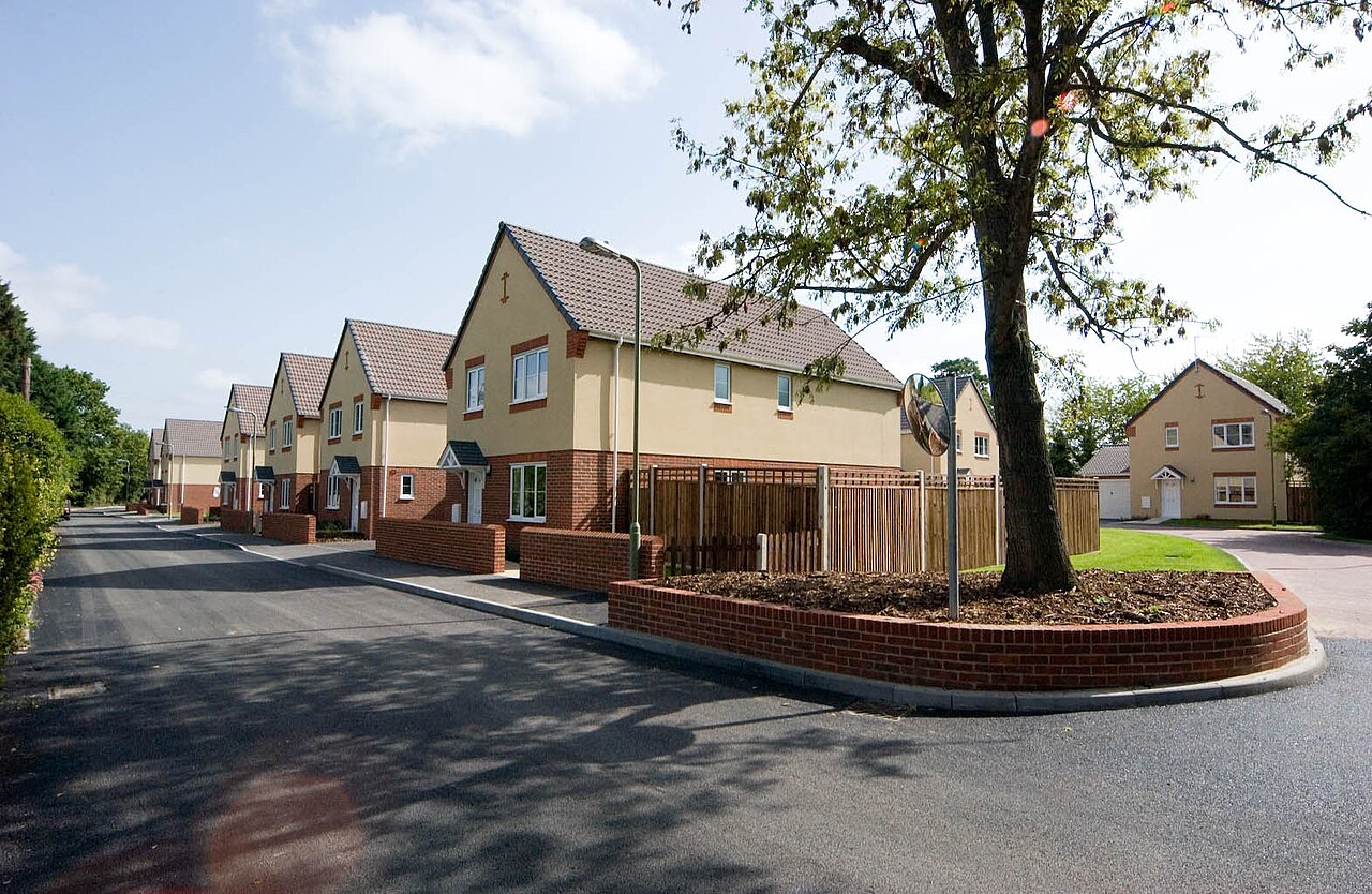 A street of modernised service family homes, with brick garden walls and a tree on a corner verge.