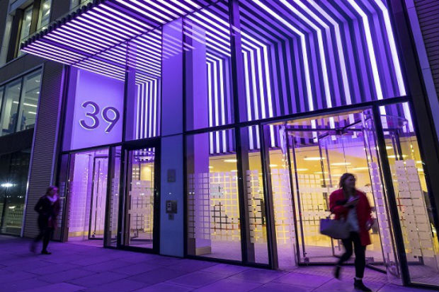 The entrance to the Department of Health and Social Care offices in London, lit in purple, with two people walking past (archive photograph from 2018)