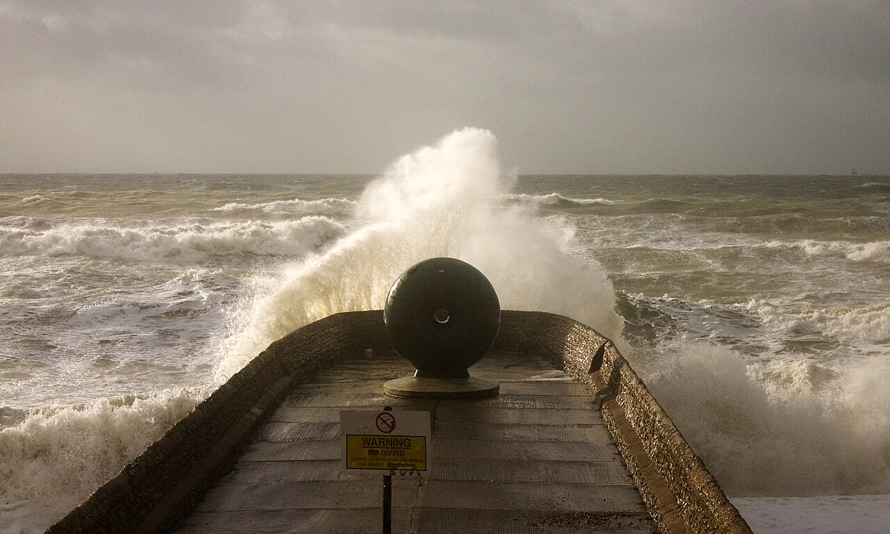 A large wave breaking over a stone breakwater on the seafront at Brighton under a grey sky, in a 2009 archive photograph