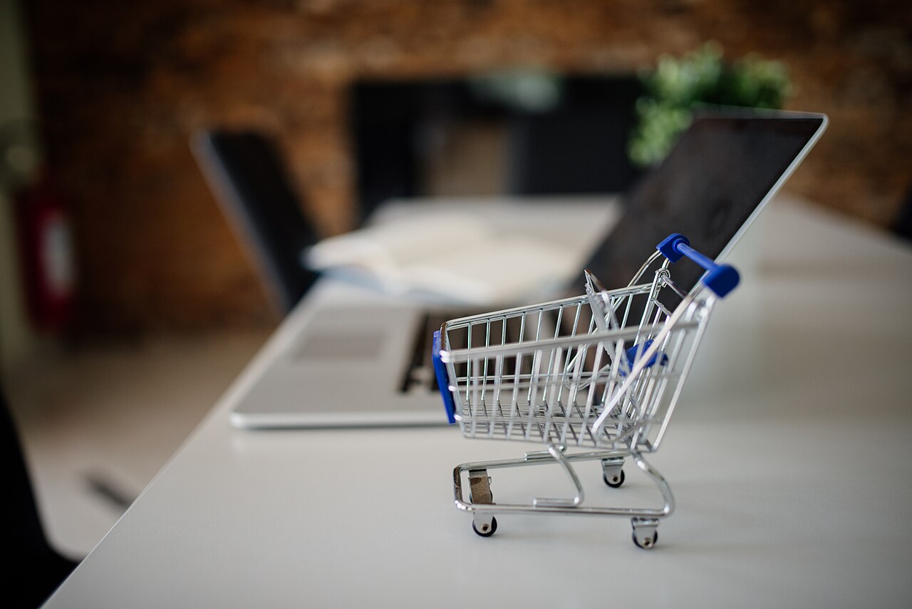 A miniature shopping trolley on a table in front of an open laptop