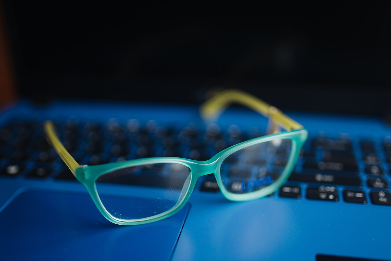 A pair of glasses resting on a laptop keyboard, with the glowing screen visible behind them