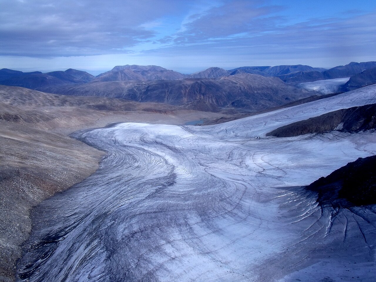 A glacier on Baffin Island, Nunavut, Canada, with curved flow lines in the ice and brown mountains behind