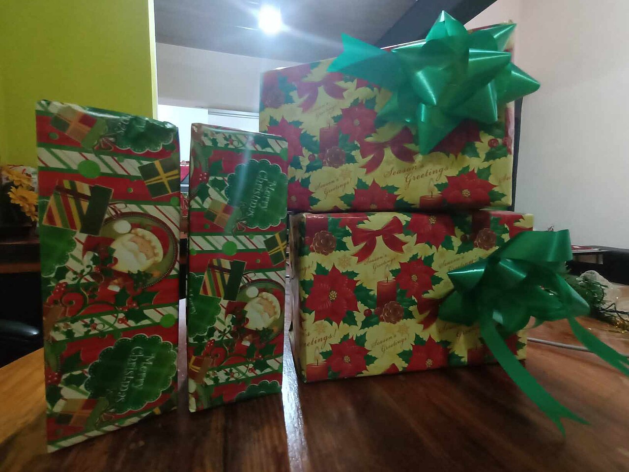 Four wrapped Christmas presents, two with green bows, on a wooden table.