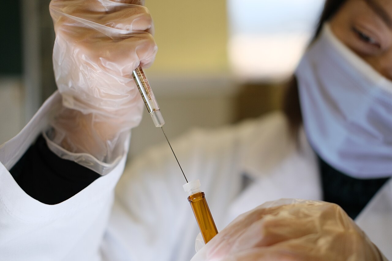 A researcher in gloves and a face mask draws liquid from a vial into a syringe