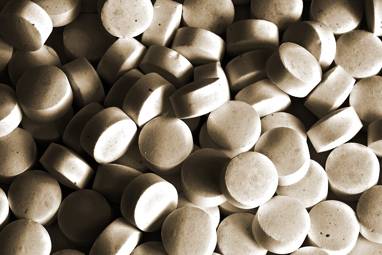 A close-up pile of round white tablets in sepia tone